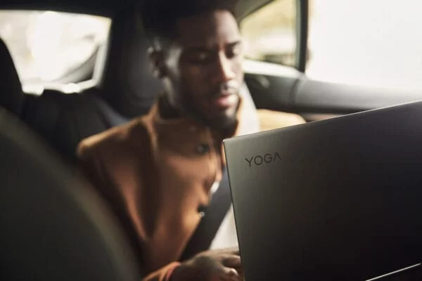 Man sitting in the backseat of a car using a Lenovo Yoga 5G laptop.