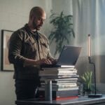 Lenovo Managed Services - person working from home with a ThinkPad on top of a stack of books.