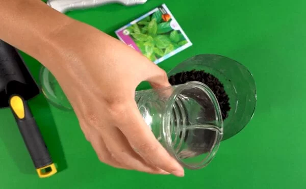 Pouring water over dirt in a DIY mini-greenhouse for STEM at Home.