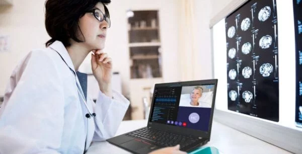 Doctor sitting with a laptop, joining a virtual consultation and reviewing body scan images.
