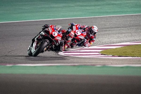 Two Ducati racers in a deep lean as they round a turn on a racetrack