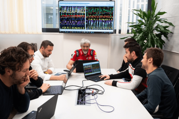 Tardozzi and team sitting around a conference room table using Lenovo devices to review data, which also streams on a monitor on the wall.