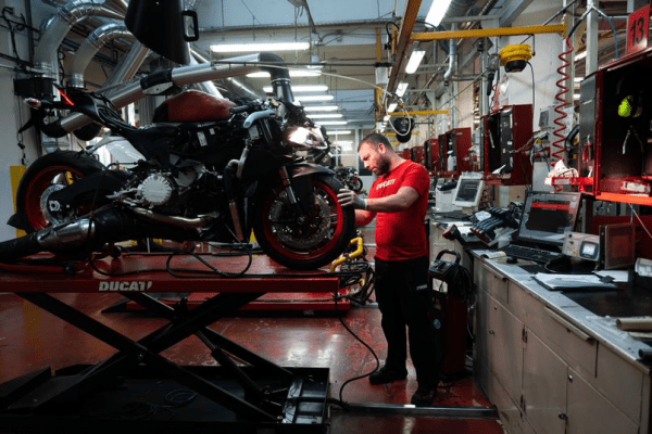 Mechanic with Ducati motorbike on elevated platform, tuning up the machine