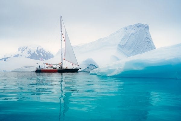 Sailboat passing by glaciers in Antarctica with bright blue water.