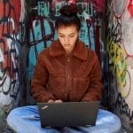 Lenovo New Realities: Germany's Jamilah Bagdach sitting outside in front of colorful graffiti working on a Thinkpad