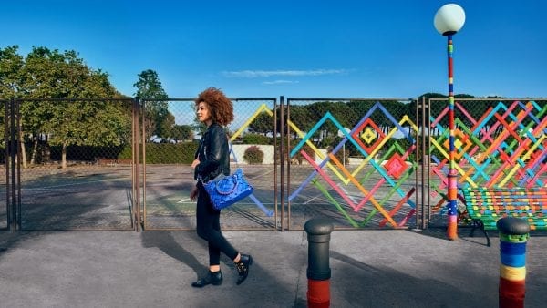 Lenovo brand image - Multicolored yarn weaving geometric shapes through a chain link fence behind a woman walking past