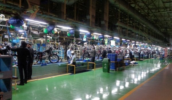 Hero MotoCorp assembly line, wide shot with multiple people working on dozens of motorcycles.