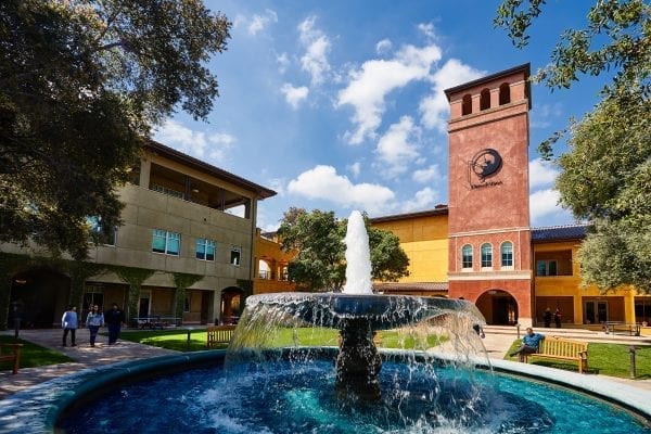 DreamWorks Animation campus with a large fountain in the foreground, people walking in the distance, and the DreamWorks logo visible on a brick building.