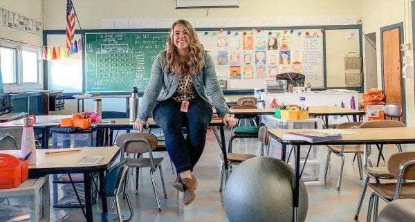 Teacher Jess Smith in an empty classroom, holding herself up between two chairs.