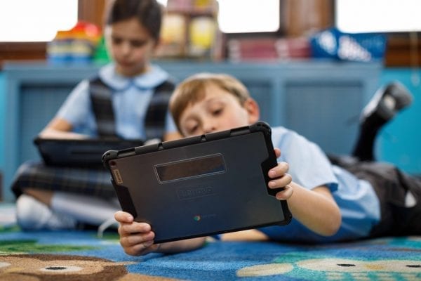 Young kid lying down and using a Lenovo tablet to learn remotely