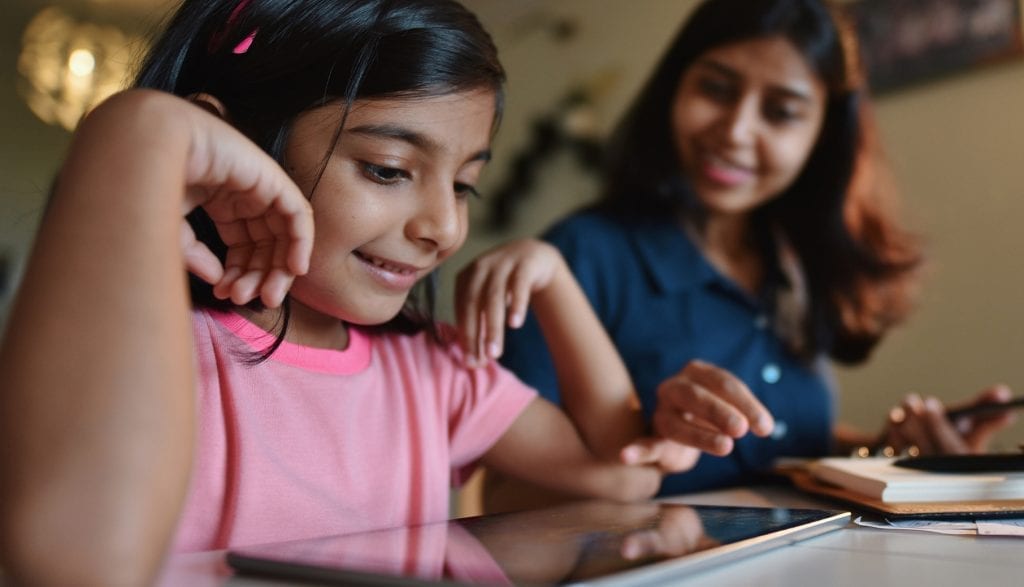 Mother looks on while daughter uses a digital tablet