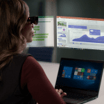 Woman wearing the ThinkReality A3 headset while sitting at a Lenovo laptop with a virtual desktop projected above