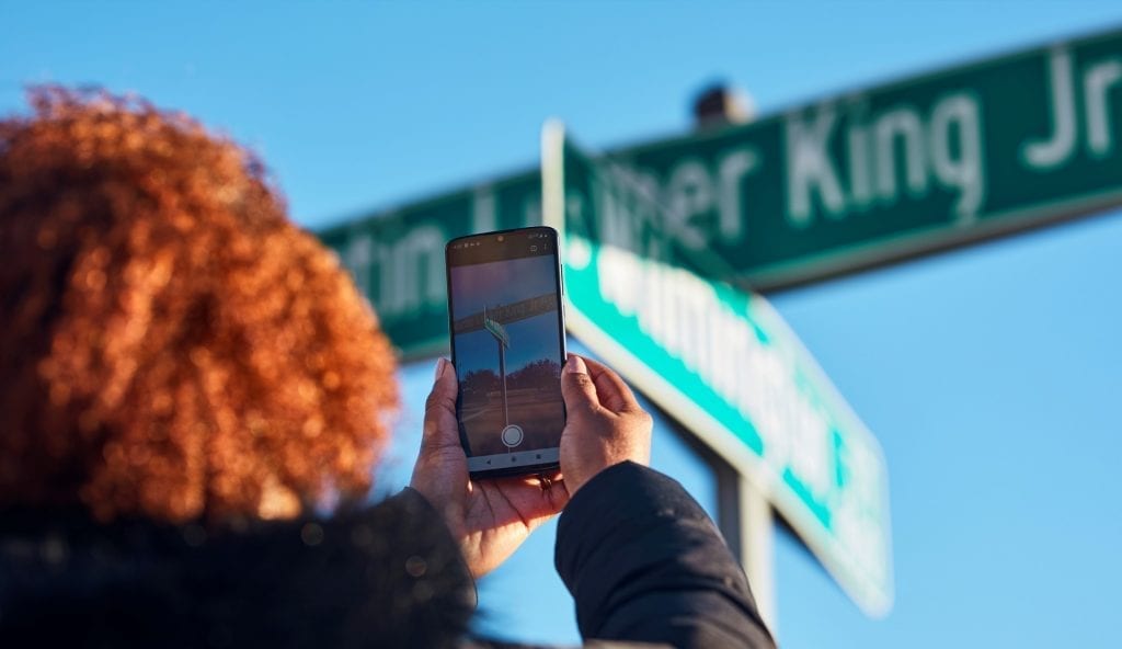 Person holding up their smartphone and aiming it at a MLK, Jr. street sign to activate the AR experience
