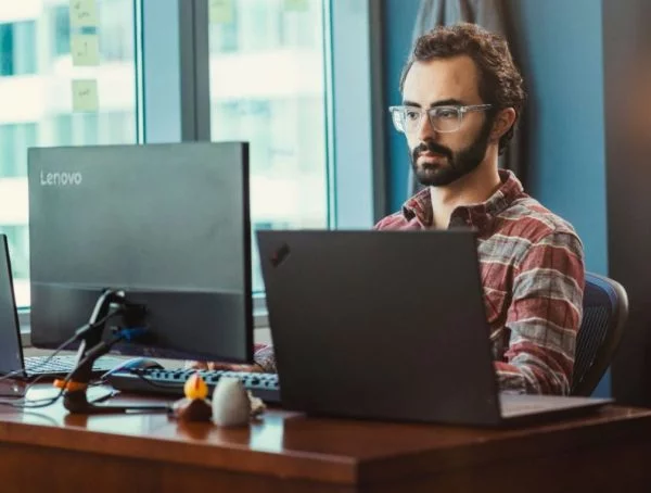 Person sitting at a desk with a Lenovo ThinkPad laptop and external monitor.