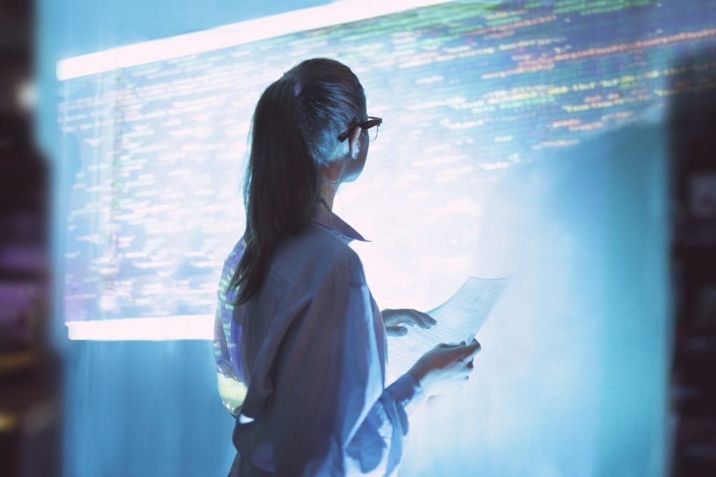 Woman in front of a detailed projection of some kind of data schematic.
