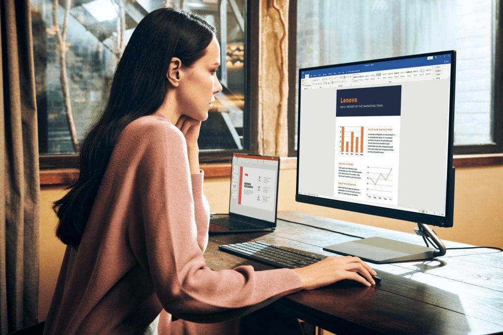 Qreator 25 monitor seen in a WFH setup with a woman leaning forward and working across two monitors.