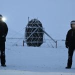 Sebastian and Karl wearing insulated suits and helmets standing in front of the Lunark module in Greenland, surrounded by snow.