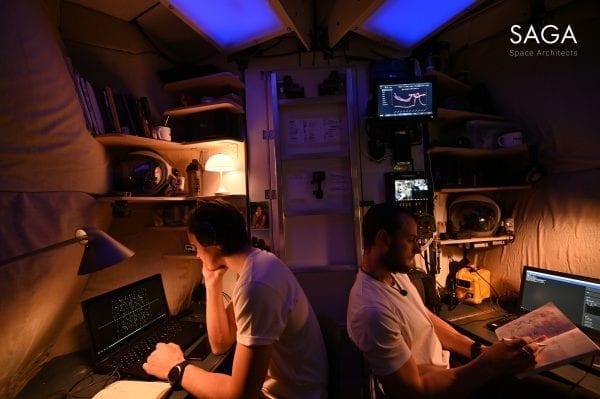 Sebastian and Karl in the module at night, sitting at different workstations with multiple monitors.