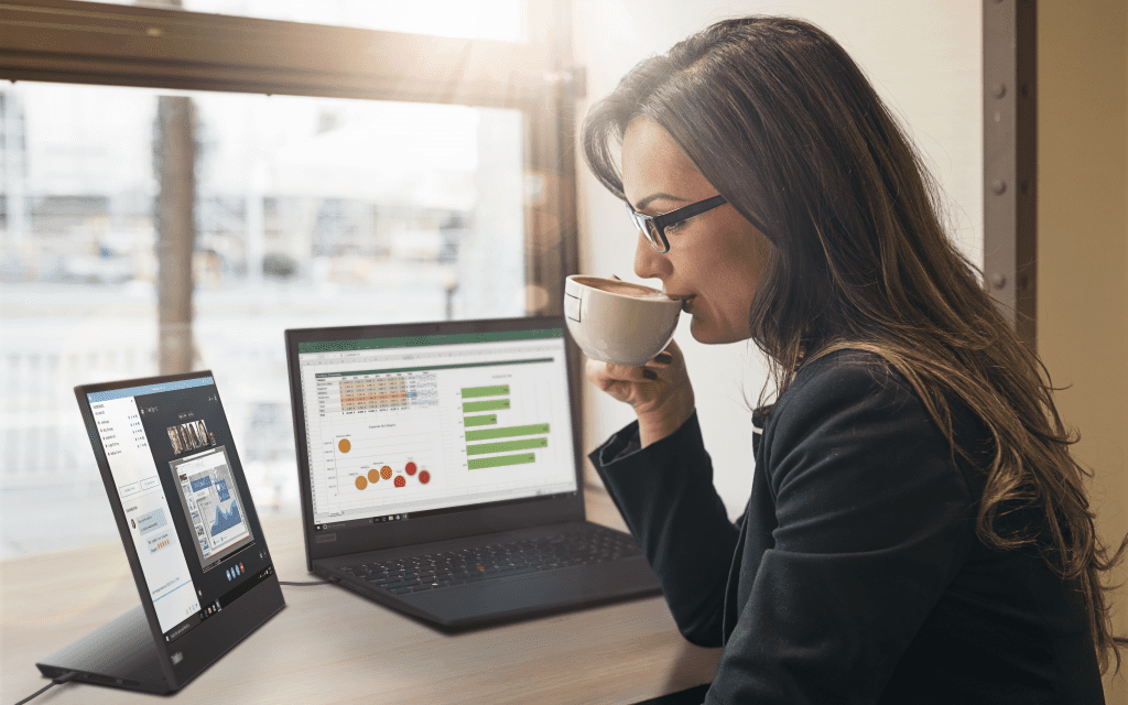 Woman reviewing content on ThinkVision M15 mobile monitor while sipping coffee