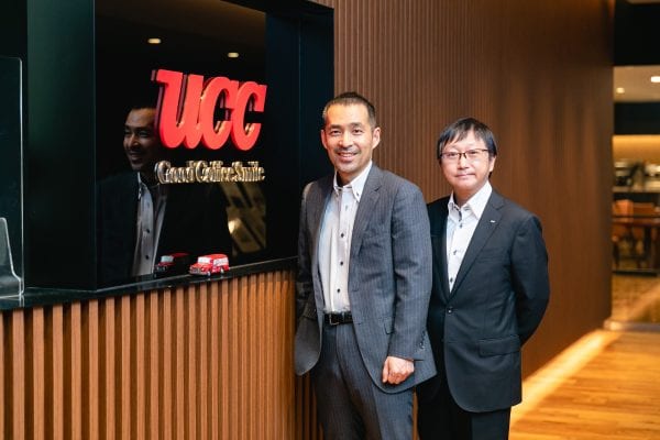 Two executives standing in front of UCC Holdings, a Japanese coffee-maker, sign