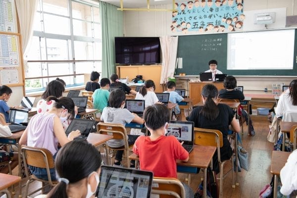 Wide shot of students in a Japanese classroom, wearing masks and using Lenovo PCs