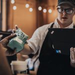 321 Coffee employee passing a bag of coffee to a customer while using a Lenovo ThinkPad