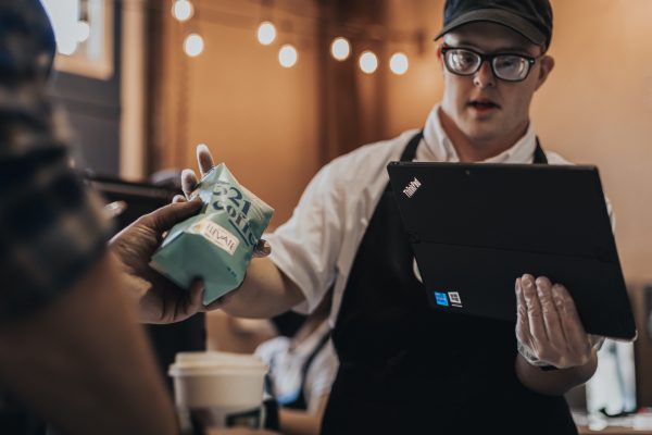 321 Coffee employee passing a bag of coffee to a customer while using a Lenovo ThinkPad