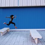 brand image - Athletic young woman leaping over concrete benches outside.