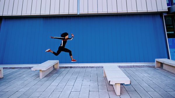 brand image - Athletic young woman leaping over concrete benches outside.