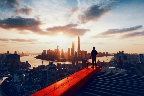 Brand image - person standing on red walkway looking out over sunrise on a city skyline