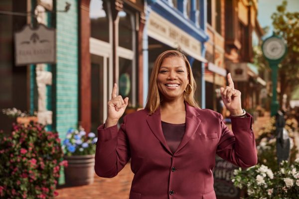 Queen Latifah outside, smiling and pointing fingers to the sky