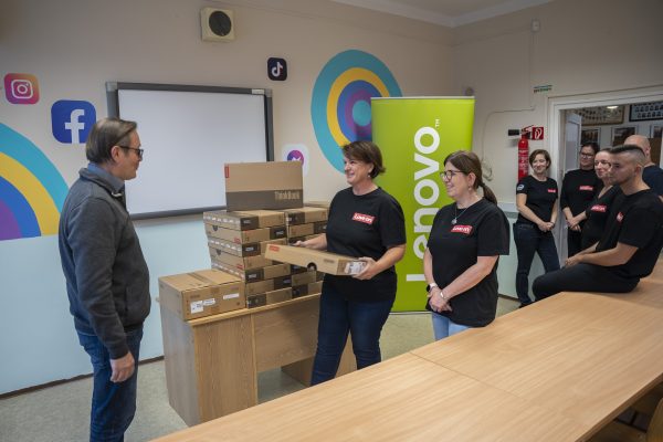Teacher being presented with new laptops in boxes by Lenovo team in branded tops in classroom