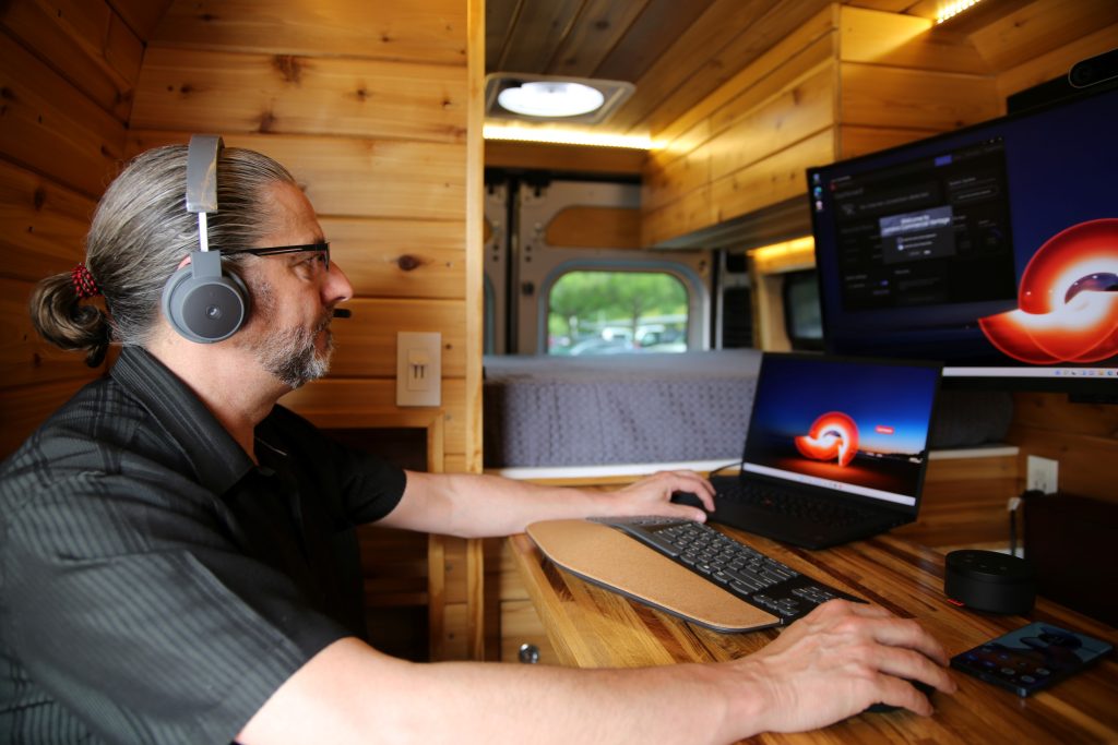 Someone working on a computer with external accessories inside the van.