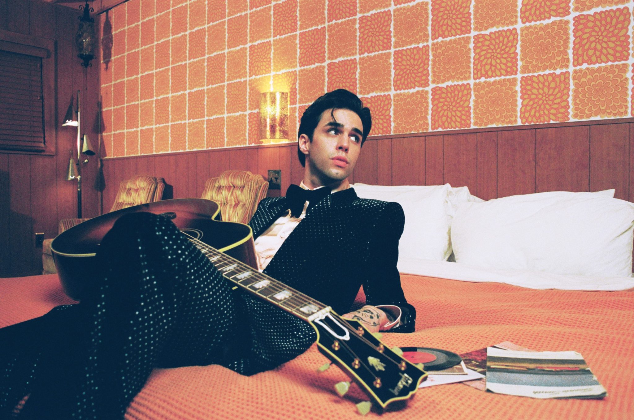 Stephen Sanchez reclining on a bed with a guitar across his lap