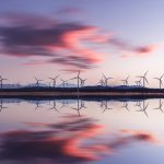Field of wind turbines at sunset reflected in water.