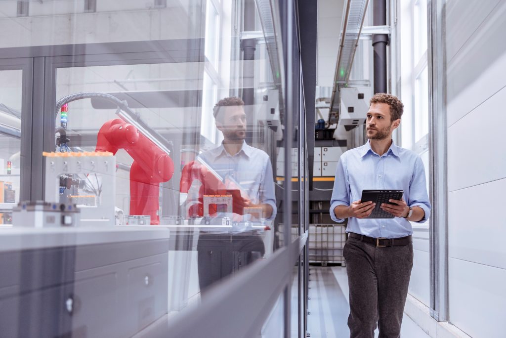 brand image - person walking down a hallway with a device, looking through window at manufacturing equipment