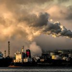 Industrial landscape with cargo ship and plumes of cloud emissions into the sky