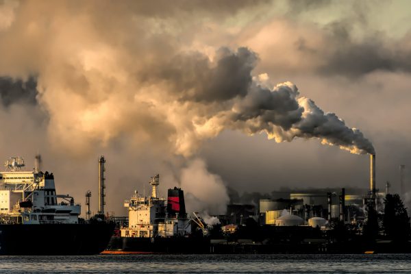 Industrial landscape with cargo ship and plumes of cloud emissions into the sky