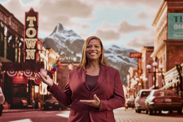 Queen Latifah standing on a small-town main street with a mountain in the distance.