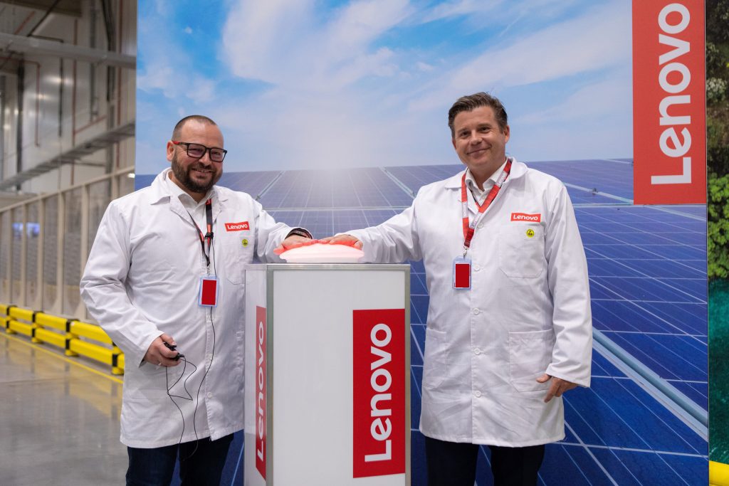 Two men in white lab coats pressing a button on a plinth smiling next to Lenovo logo