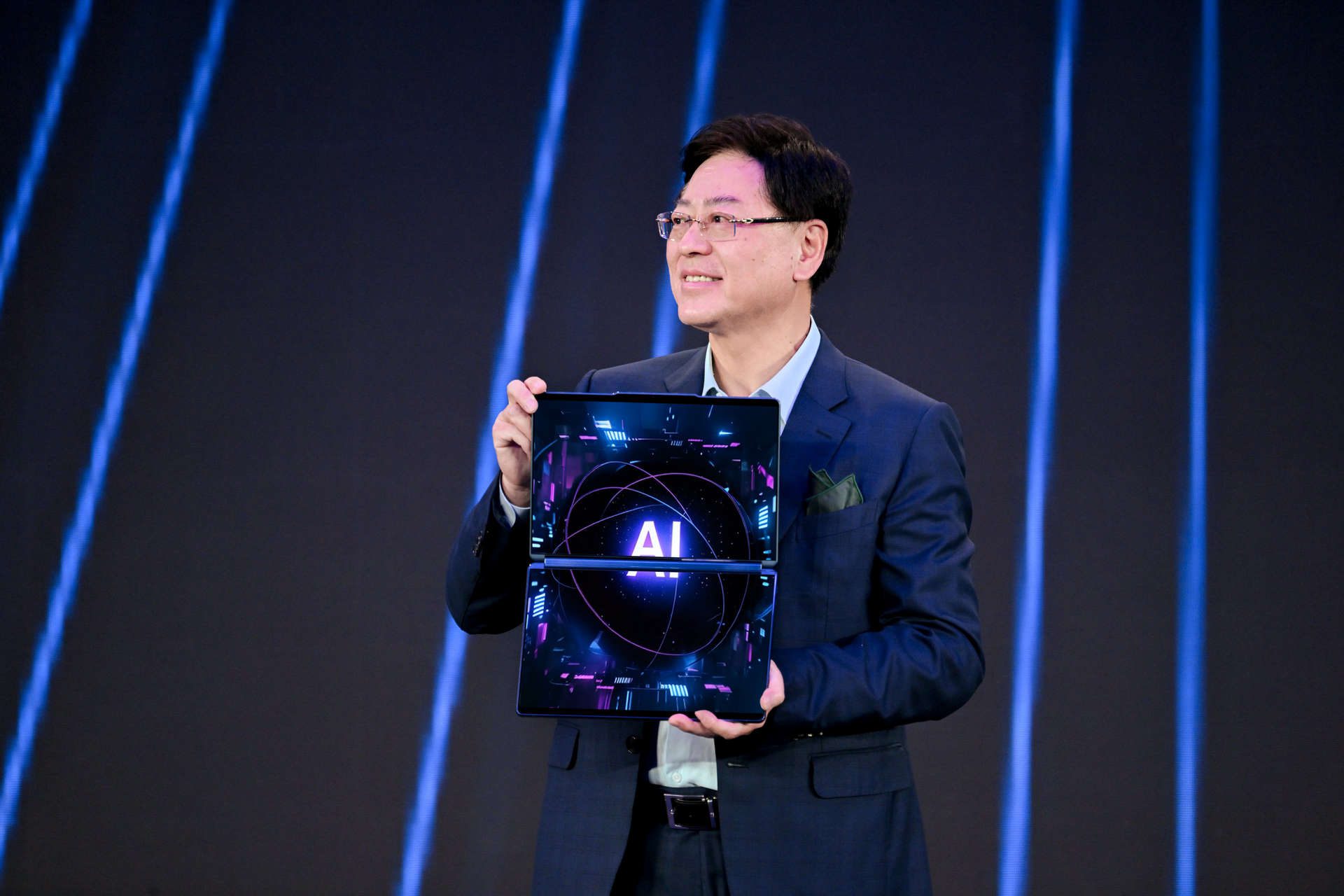 Yuanqing Yang on stage at at Tech World Shanghai holding a dual-screen laptop