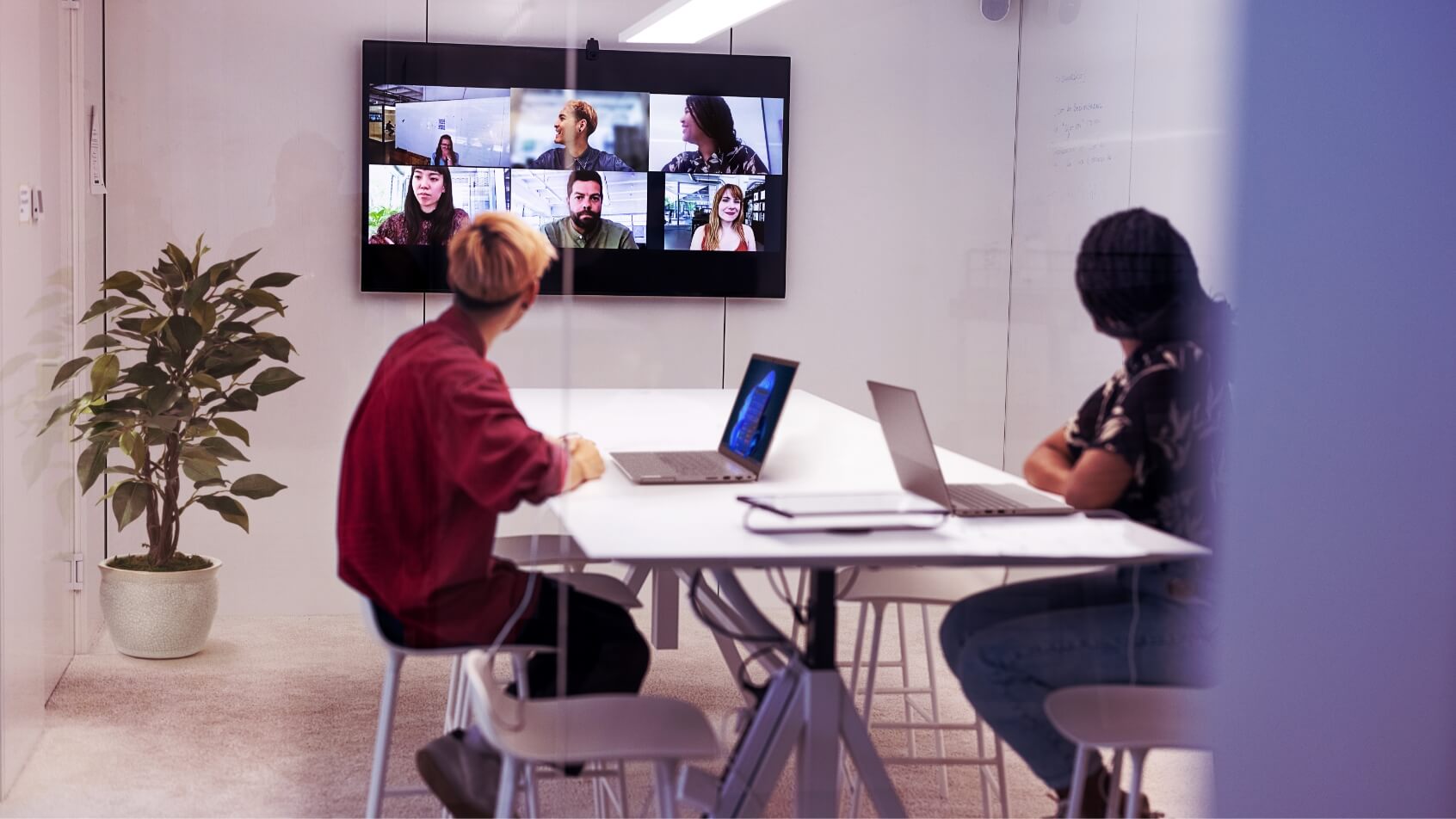 Two people in a meeting room having a video conference with six other participants
