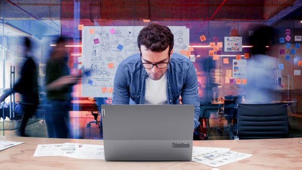 Brand image - person working at table with ThinkBook, people passing by in the background.